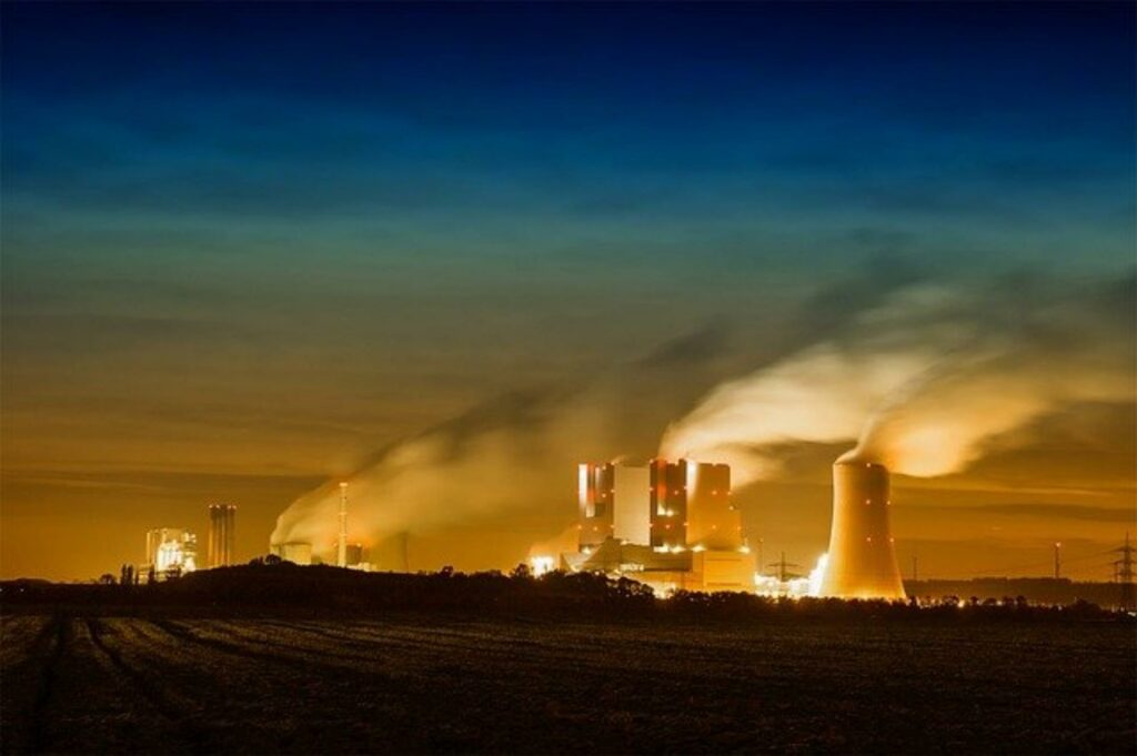 Rauchende Schlote und Kühltürme eines Kohlekraftwerks bei Nacht
