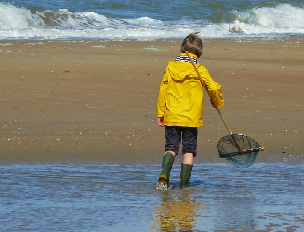 Ein Kind in Wetterkleidung vergnügt sich an einem Strand - die Regenjacke ist imprägniert mit giftigen PFAS-Chemikalien